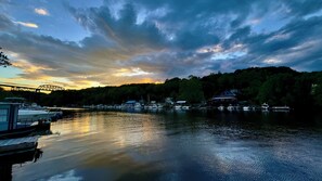 Um rio calmo com barcos atracados à esquerda, uma ponte ao fundo e um edifício iluminado à direita.