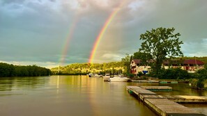 Ein ruhiger See mit Regenbogen, angestaute Booten und Häusern im Hintergrund.