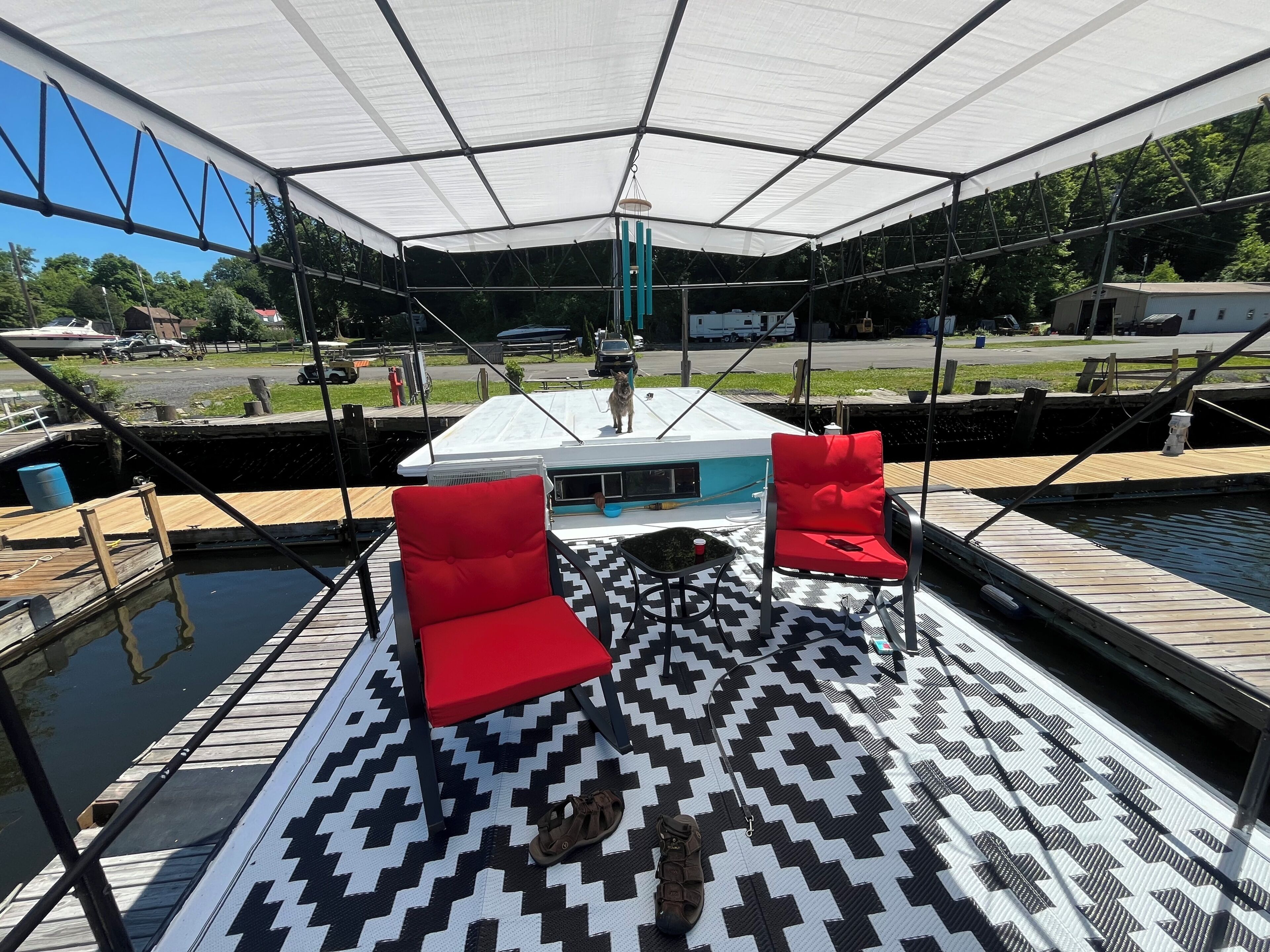 Eine überdachte Terrasse mit zwei roten Stühlen, einem gemusterten Teppich und einem im Hintergrund liegenden Boot.