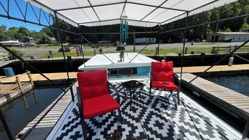 Eine überdachte Terrasse mit zwei roten Stühlen, einem gemusterten Teppich und einem im Hintergrund liegenden Boot.
