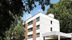 Moderni rakennus, jossa on katettu sisäänkäynti, suuret ikkunat ja pysäköintialue.