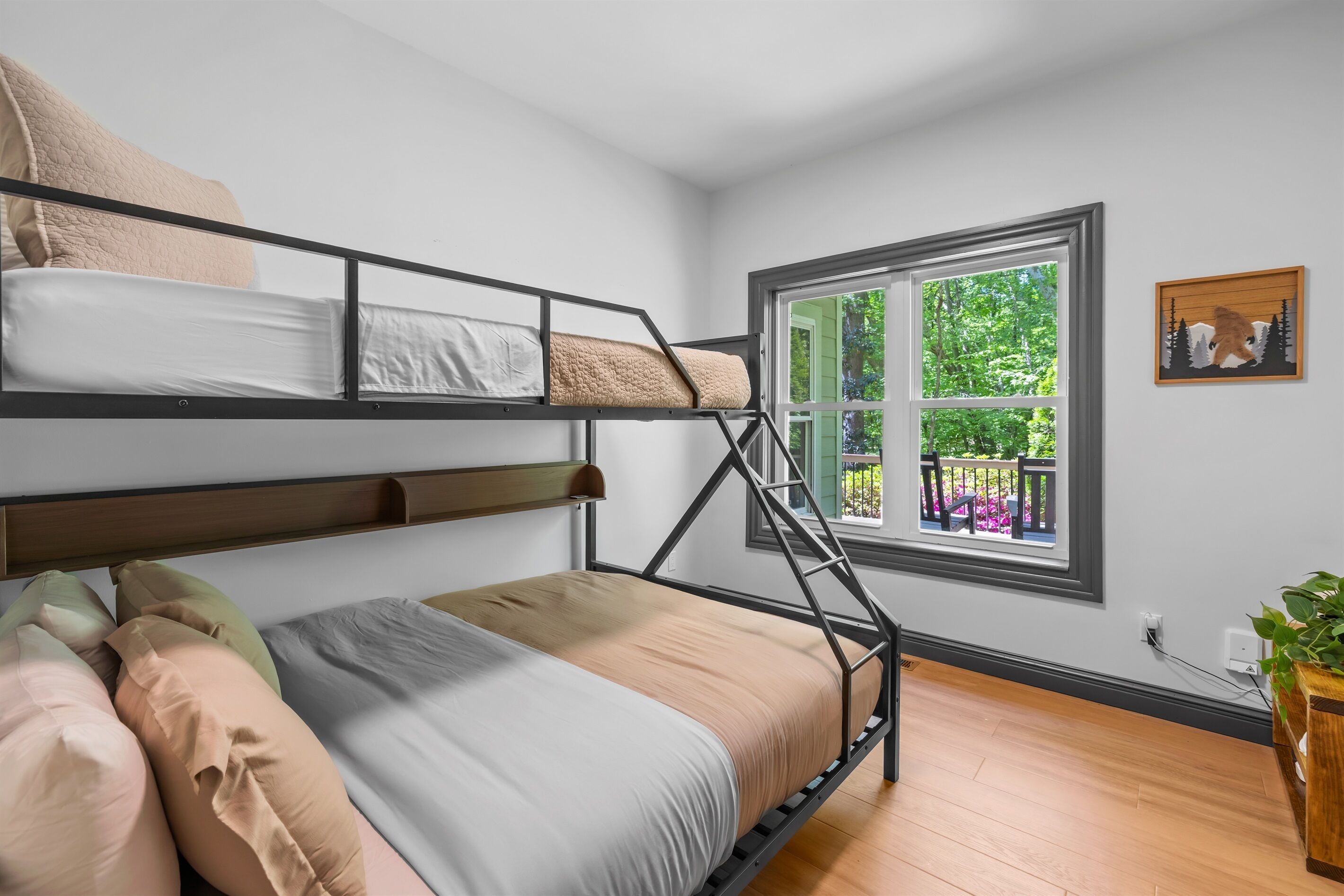 Habitación con literas y vista a la vegetación, suelo de madera y una planta pequeña a la derecha.
