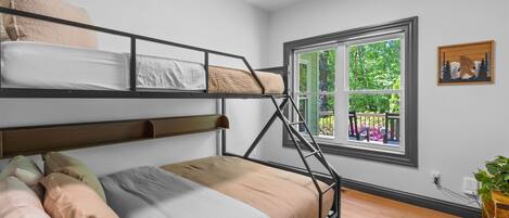 Habitación con literas y vista a la vegetación, suelo de madera y una planta pequeña a la derecha.