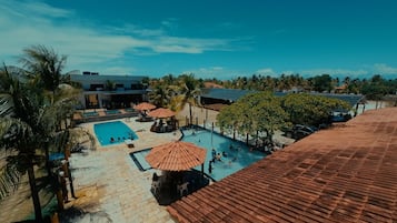 A rooftop pool area with multiple pools, umbrellas, and palm trees.