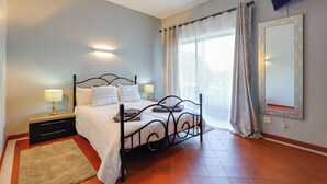 A bedroom with a bed, bedside tables, a TV, and a window with curtains. - Golden Grandfather's Corner (Albufeira)