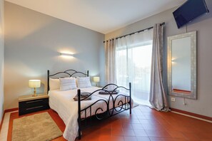 A bedroom with a bed, bedside tables, a TV, and a window with curtains. - Golden Grandfather's Corner (Albufeira)