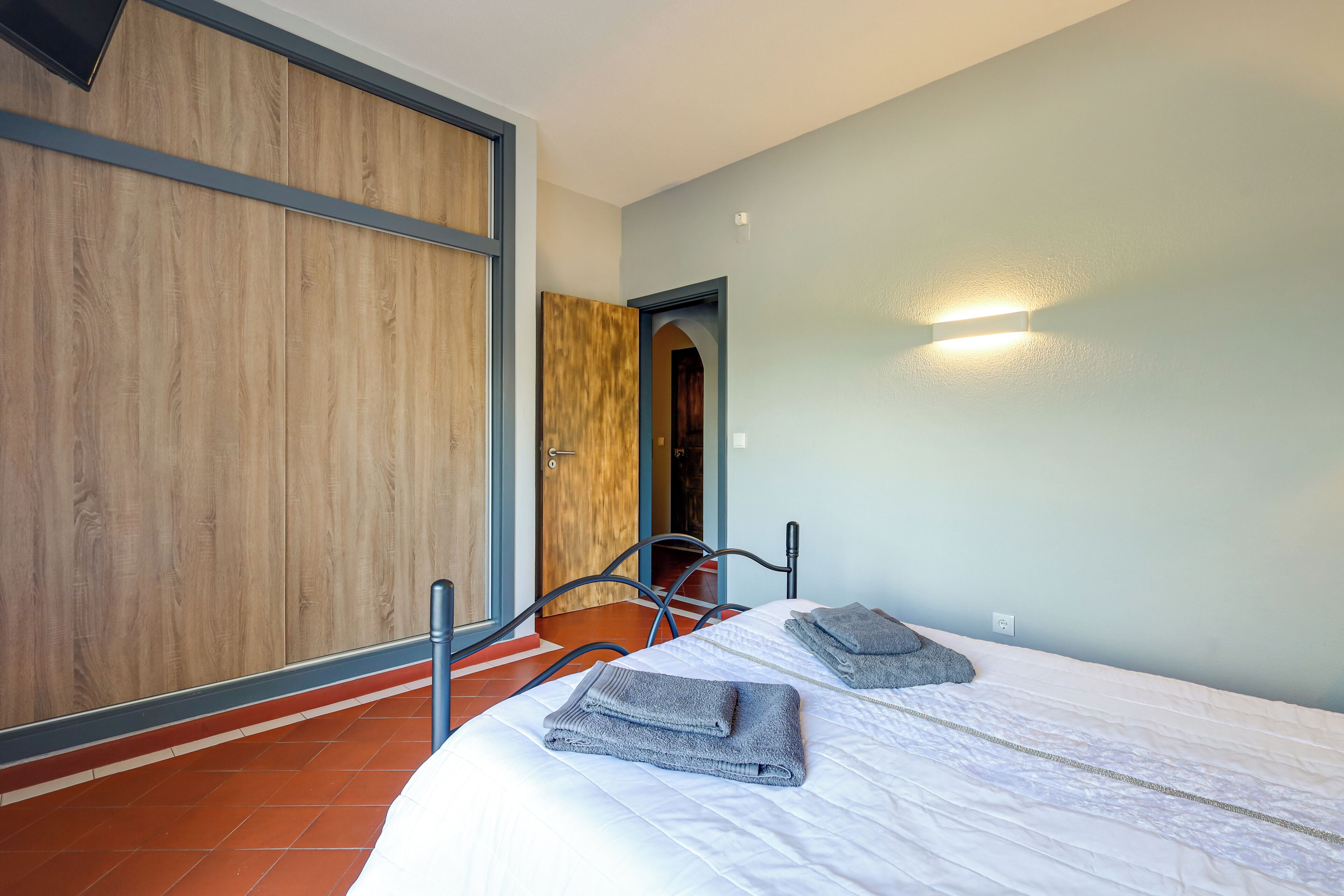 Een kamer met een bed, een houten garderobe, een deur en een wandlamp.