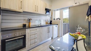 A modern kitchen with wooden cabinets, stainless steel appliances, and a dining area with a table and chairs. - Golden Grandfather's Corner (Albufeira)