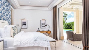 A bedroom with a bed, a desk, and a view of a swimming pool. - Villa Tamarindo - by Zenbreak (Holetown)
