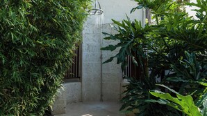 A concrete shower area with a metal faucet, surrounded by dense green foliage. - Villa Tamarindo - by Zenbreak (Holetown)