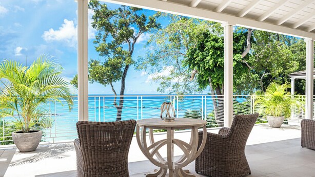 A covered outdoor seating area with wicker furniture, a round table, and a view of the sea. - Villa Tamarindo - by Zenbreak (Holetown)