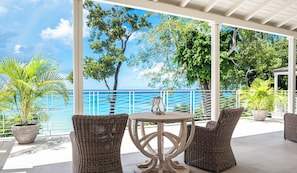 A covered outdoor seating area with wicker furniture, a round table, and a view of the sea.