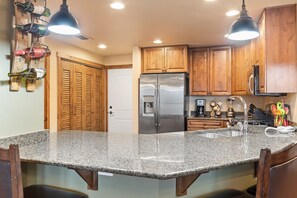 A kitchen with wooden cabinets, a stainless steel refrigerator, granite countertops, and pendant lighting. - Newly Listed Luxury Whitefish Vacation Rental with Amazing Amenities (Whitefish)