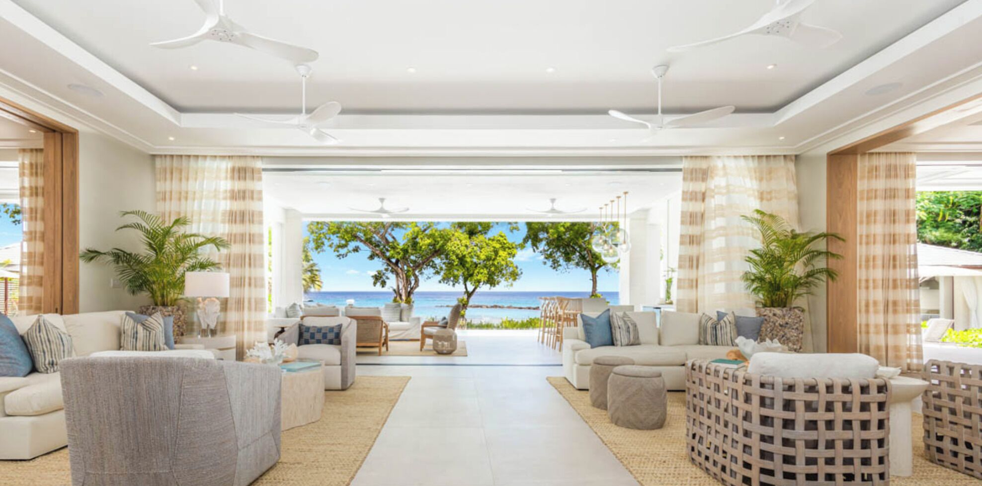 A spacious living area with a view of the ocean, furnished with sofas and chairs, and featuring ceiling fans.
