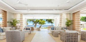 A spacious living area with a view of the ocean, furnished with sofas and chairs, and featuring ceiling fans. - One Beachlands - by Zenbreak (Holetown)