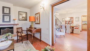 Een woonkamer met een open haard, een eethoek met een tafel en stoelen, en een trap naar een hoger gelegen verdieping.