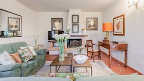 Een woonkamer met een bank, salontafel, open haard, televisie en ingelijste foto's aan de muur.
