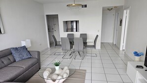 Una sala de estar moderna con un sofá gris, una mesa de centro de vidrio y un comedor con sillas grises y una mesa blanca.