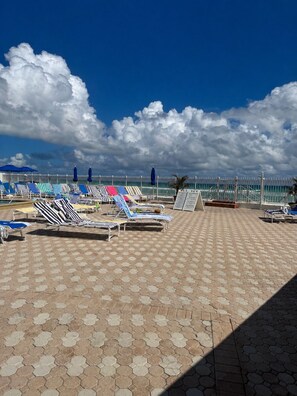 Ein Strandloungebereich mit sechseckig gefliestem Boden, Liegestühlen und Sonnenschirmen.