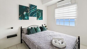 A bedroom with a bed, air conditioning, a window with blinds, and artwork on the wall. - Modern retreat close to Trinidad's best sites. (Port of Spain)