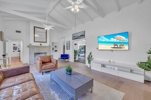 Ein geräumiges Wohnzimmer mit Kamin, Ledersofa und einem großen Fernseher, der eine Strandansicht zeigt.