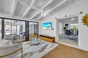 Ein modernes Wohnzimmer mit Glastür zum Balkon, einem an der Wand befestigten Fernseher und einem Deckenventilator.