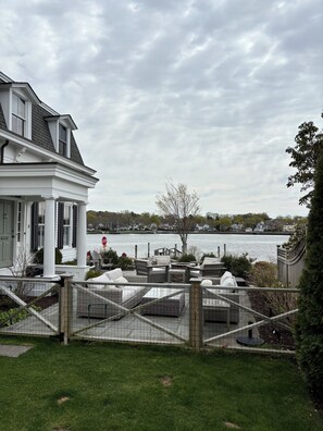 Une propriété située au bord de l’eau, dotée d’un patio couvert, offrant une vue sur l’eau et comprenant une maison blanche avec un porche.