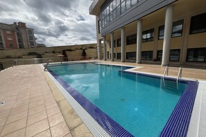A swimming pool with tiled edges, a tiled deck, and a building with columns and windows in the background. - Desconectaengalicia Pinamar with swimming pool, 50m Silgar Beach (Pontevedra)