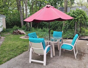 A patio with a glass table and four chairs, each with a teal cushion. A red umbrella provides shade. - Cosy Retro 2 bedroom Cottage in vibrant Broad Ripple Village Indianapolis (Indianapolis)