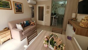 Una sala de estar con un sofá, una mesa de comedor con un centro de mesa floral, y un área de cocina al fondo.