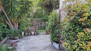 Un sendero en un jardín que lleva a un edificio, rodeado de diversas macetas con plantas y una valla de madera.