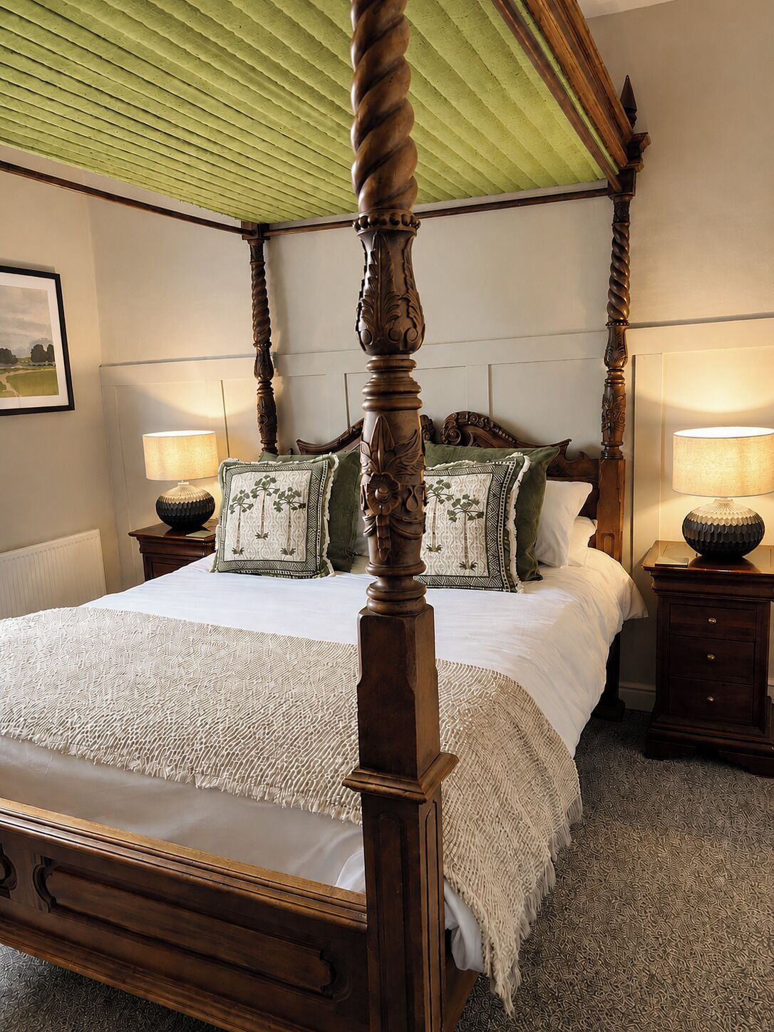 A four-poster bed with a green ceiling, two bedside lamps, and a framed picture on the wall.
