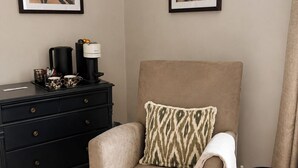Un fauteuil beige agrémenté d’un coussin à motifs, une table basse noire, une commode noire et, au mur, deux tableaux représentant des cerfs, encadrés.