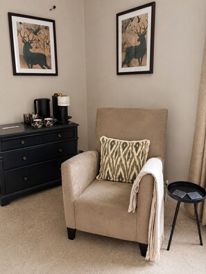 Ein beiger Sessel mit einem gemusterten Kissen, ein schwarzer Couchtisch, eine schwarze Kommode und zwei gerahmte Hirschbilder an der Wand.