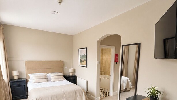 Une chambre d’hôtel comprenant un lit, un bureau, une chaise, une commode, un miroir et une petite table avec des tasses et une assiette.