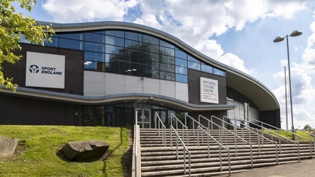 Un edificio moderno con fachada curva, un cartel de Sport England y un cartel del National Cycling Centre.