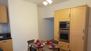 Una cocina compacta con armarios de madera, una mesa de comedor con sillas y electrodomésticos integrados.