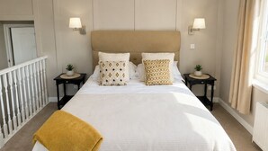 A large bed with a beige headboard, two bedside tables with lamps, and a window with curtains. - Raven Suite - 4 | Central Location (Shropshire)