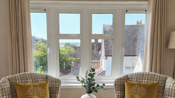 A room with two plaid armchairs, a small table with a vase, and a window with curtains. - Raven Suite - 4 | Central Location (Shropshire)
