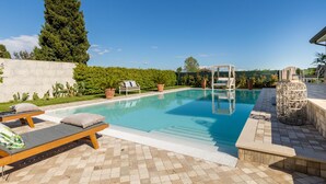 En pool med solstolar, en pergola och en stenmur.
