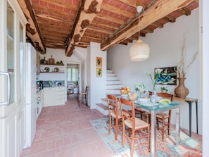 Una cocina amplia con armarios blancos, un comedor con mesa de vidrio y una escalera que sube a otro nivel.