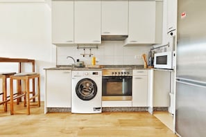 Eine Küche mit weißen Schränken, einer Waschmaschine, einem Backofen, einer Mikrowelle und einem Edelstahl-Kühlschrank.