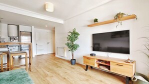 Ein modernes Wohnzimmer mit Holzboden, einem grünen Sofa, einem Fernseher, einem Holzschrank und einer Zimmerpflanze.