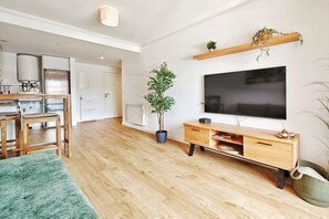 A modern living room with a wooden floor, a green sofa, a TV, a wooden cabinet, and a potted plant. - Desconectaengalicia Mar de Silgar 600m Silgar beach (Pontevedra)