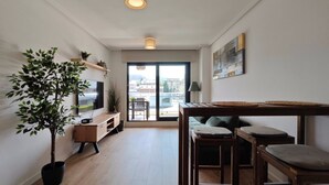 Ein modernes Wohnzimmer mit Fernseher, Holzmöbeln, einer großen Kübelpflanze und Blick durch eine Glastür.