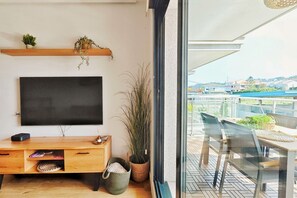 Ein modernes Wohnzimmer mit Flachbildfernseher, einer Holztrennwand, Topfpflanzen und einem Balkon mit Sitzgelegenheit.