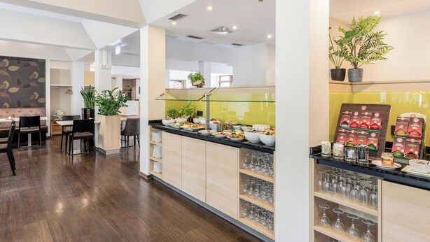 Un moderno hall de hotel con zona de comedor, mostrador de recepción y mesa de buffet.