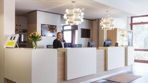 Un mostrador de recepción de hotel con una recepcionista, una pantalla digital y un ventanal grande.