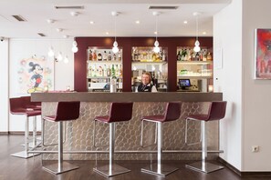 A bar area with a bartender, bar stools, and a variety of liquor bottles. - Select Hotel Osnabruck (Osnabrueck)