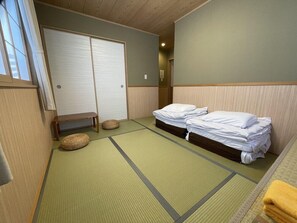 Una habitación con esteras de tatami, dos camas, un banco y un armario.